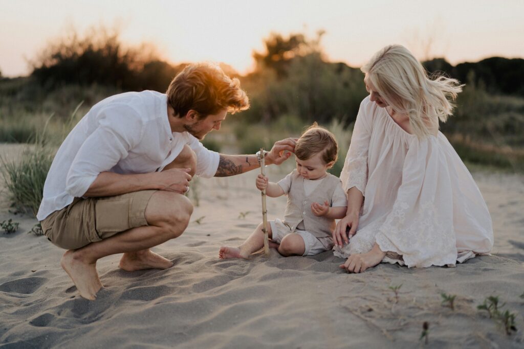 A family with a toddler enjoying a peaceful moment on a beach at sunset.