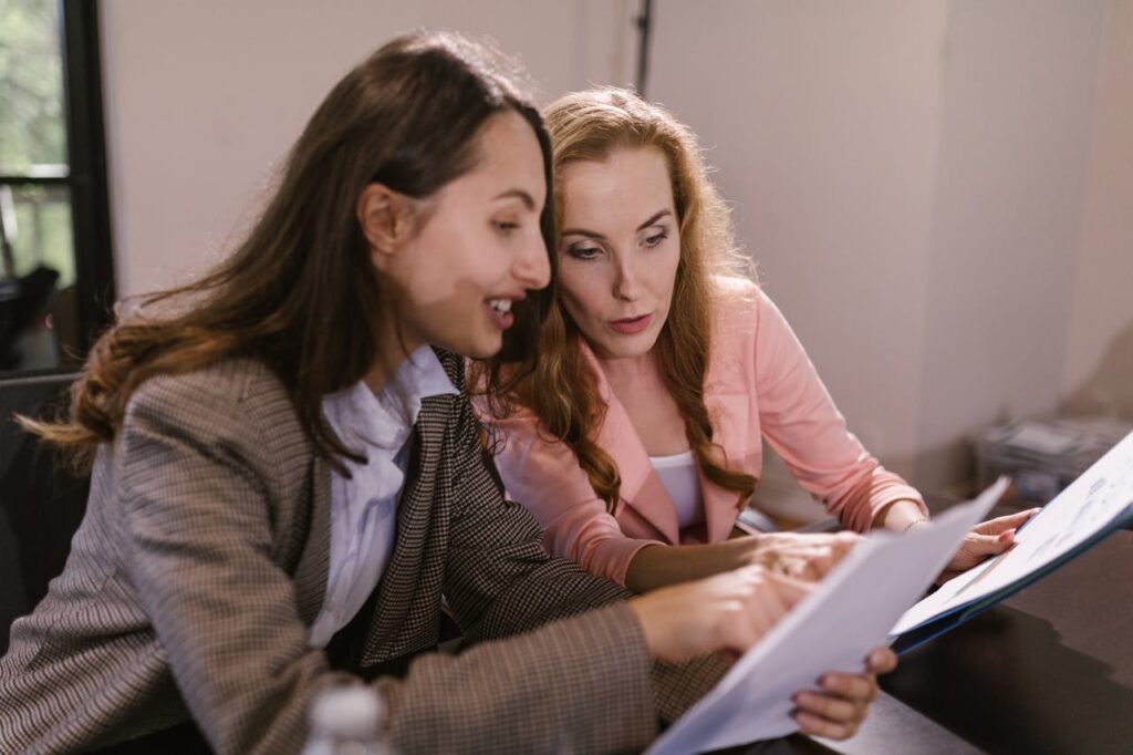 Two businesswomen discussing documents during an indoor meeting, showcasing teamwork and collaboration.