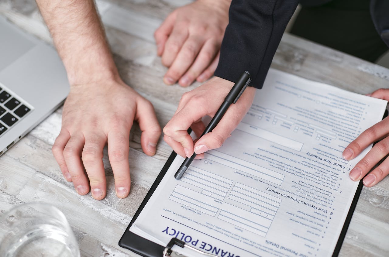 Close-up image of two people signing an insurance policy document on a wooden desk.